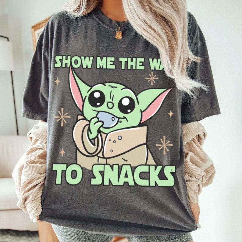 Peut inclure: T-shirt gris fonc&eacute; avec un personnage de dessin anim&eacute; vert tenant un petit objet bleu. Le texte "SHOW ME THE WA" et "TO SNACKS" est imprim&eacute; en vert. Le design comprend des &eacute;toiles et des diamants. V&ecirc;tement d&eacute;contract&eacute;.