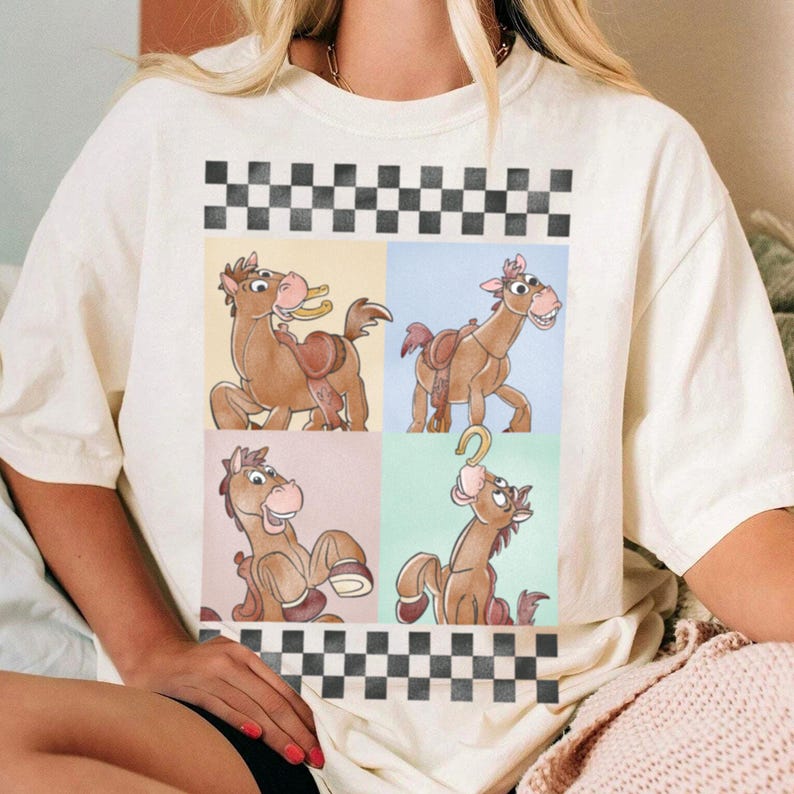 May include: Off-white t-shirt featuring a four-panel design of a cartoon horse with a saddle and a horseshoe. The panels are set against pastel backgrounds and framed by a black and white checkered pattern.