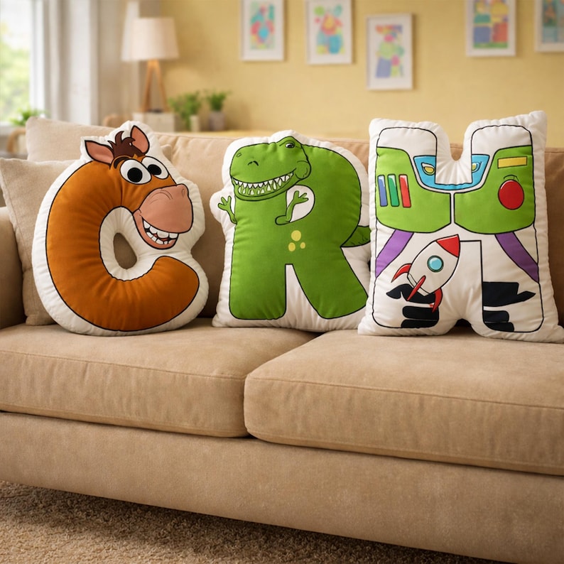 Puede incluir: Tres cojines decorativos con forma de las letras G, R y H. El coj&iacute;n G es marr&oacute;n y tiene forma de caballo. El coj&iacute;n R es verde y tiene forma de dinosaurio. El coj&iacute;n H es blanco con un dise&ntilde;o de Buzz Lightyear.