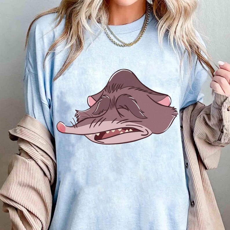 Peut inclure: T-shirt bleu clair avec un dessin anim&eacute; de rat grincheux. Le rat a les yeux ferm&eacute;s, un long nez et des dents visibles. Il est principalement marron avec des d&eacute;tails roses. Le t-shirt est en mati&egrave;re douce et convient &agrave; un usage quotidien.