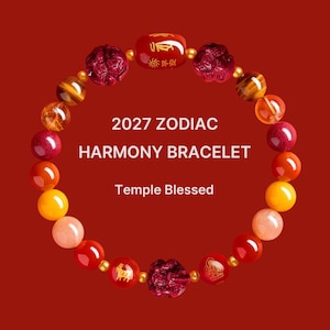 May include: A circular beaded bracelet featuring multicolored gemstone beads, two red carved floral-shaped beads, and a central red cylindrical bead with gold text. The text 2027 ZODIAC HARMONY BRACELET Temple Blessed is centered within the bracelet loop.