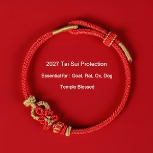 May include: A red cord bracelet featuring gold-colored thread accents and a central decorative knot. The text 2027 Tai Sui Protection, Essential for: Goat, Rat, Ox, Dog, Temple Blessed is printed in the center of the circular bracelet.