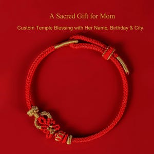 Può includere: Un braccialetto rosso intrecciato con dettagli dorati. Il braccialetto presenta un'intricata lavorazione a nodi e dettagli dorati decorativi. Il testo sull'immagine recita "A Sacred Gift for Mom" e "Custom Temple Blessing with Her Name, Birthday & City".