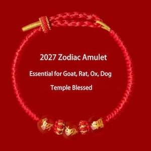 May include: A red braided cord bracelet featuring three red beads with gold-colored animal engravings and two small gold-colored cylindrical accents. The text 2027 Zodiac Amulet, Essential for Goat, Rat, Ox, Dog, Temple Blessed is centered.