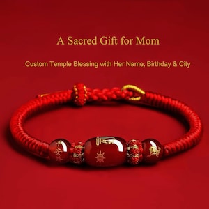 Puede incluir: Pulsera trenzada roja con detalles dorados y tres cuentas centrales. La cuenta central es un óvalo rojo oscuro con símbolos dorados. Se muestra el texto "A Sacred Gift for Mom" y "Custom Temple Blessing with Her Name, Birthday & City".