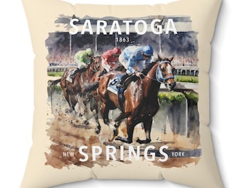 May include: A beige throw pillow with a watercolor illustration of horses racing at Saratoga Springs, New York. The text "SARATOGA 1863 NEW SPRINGS YORK" is printed on the pillow.