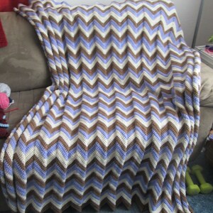 May include: A brown, white, and purple chevron patterned crocheted throw blanket draped over a couch.