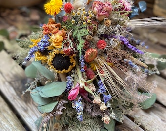 May include: A dried flower bouquet with sunflowers, roses, lavender, and eucalyptus leaves. The bouquet is arranged in a rustic style and has a natural, earthy feel.
