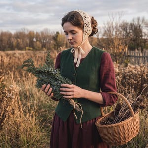 May include: A person wearing a dark green vest over a long-sleeved maroon dress, paired with a cream-colored crocheted bonnet. The person holds a bundle of green pine branches and carries a woven wicker basket filled with brown pine cones.