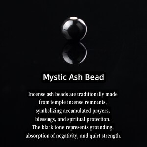 May include: A glossy, black Mystic Ash Bead, reflecting on a dark surface. The image includes text describing the bead's symbolism: grounding, protection, and strength. The bead is made from temple incense remnants.