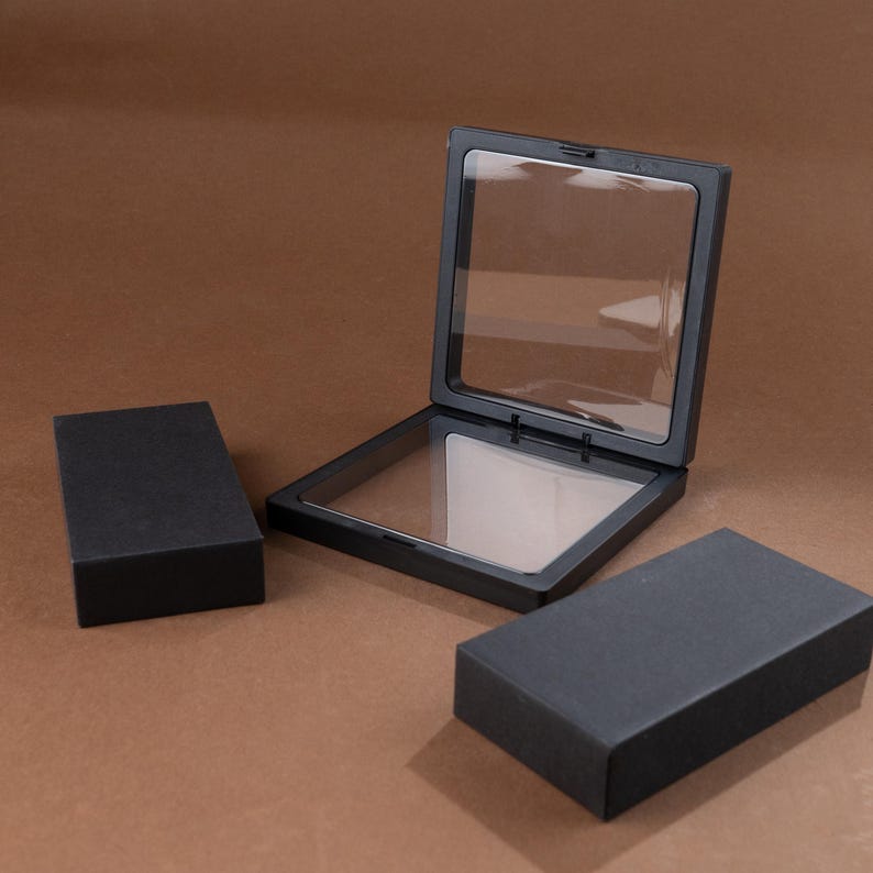 May include: Black display case with a clear window, open to reveal the interior. Two additional black rectangular boxes are also present. The items are set against a brown background.