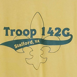 May include: Yellow t-shirt with a green and black graphic of a fleur-de-lis with the text "Troop 142G Stafford, VA" above it.