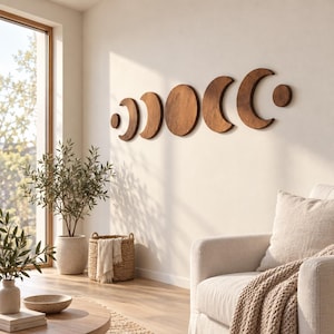 May include: A set of six dark brown wooden wall art pieces depicting the phases of the moon, arranged horizontally. The set includes a small circle, a crescent, a larger crescent, a full circle, a larger crescent, a crescent, and a small circle.