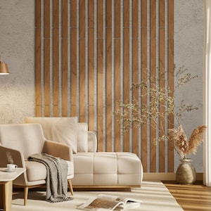 May include: A contemporary living room featuring a beige sofa, armchair, and a wooden panelled wall. A grey throw is draped over the armchair. A vase with dried plants is on the floor. A coffee table with a cup and a book complete the scene.