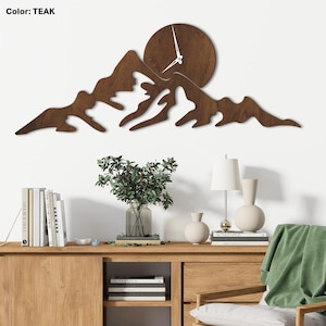 Può includere: Un orologio da parete in legno a forma di catena montuosa. Il quadrante dell'orologio è circolare con lancette bianche. L'orologio e le montagne sono di colore marrone scuro. Il testo "Color: TEAK" è in alto a sinistra.