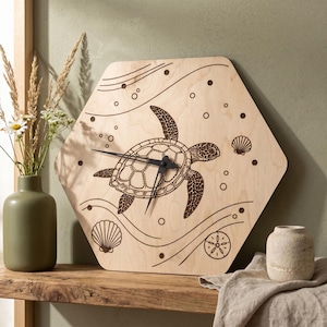 Op de afbeelding: Zeshoekige houten wandklok met een lasergeëtst ontwerp van een zeeschildpad. De klok heeft zwarte wijzers en decoratieve elementen zoals schelpen en bellen. De klok is gemaakt van lichtgekleurd hout.
