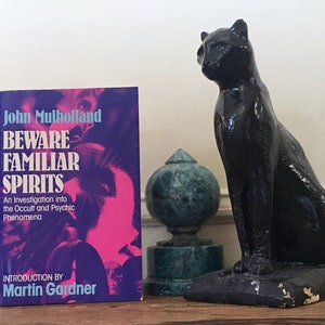 May include: A book titled "Beware Familiar Spirits: An Investigation into the Occult and Psychic Phenomena" by John Mulholland with an introduction by Martin Gardner. The book cover features a pink and purple image of a woman's face.