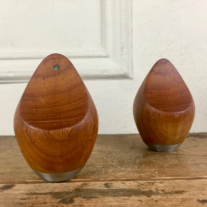 May include: Two wooden candle holders with a teardrop shape and a silver base. The candle holders are made of dark wood with a natural grain pattern.