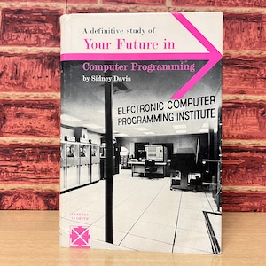 Op de afbeelding: Een boekomslag met een roze pijl die naar rechts wijst. De titel is "Your Future in Computer Programming" door Sidney Davis. De omslag toont ook een zwart-witfoto van een computerlab met een bord waarop "Electronic Computer Programming Institute" staat.