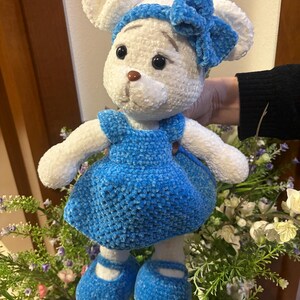 Può includere: Topolino di peluche bianco lavorato a uncinetto con un vestito blu e una fascia per capelli con un fiocco blu. Il giocattolo ha occhi neri e un naso marrone.