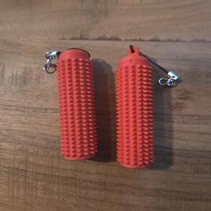 May include: Two red cylindrical massage tools with a textured, spiky surface. Each tool has a small silver clasp and a black cord attached. The tools are designed for muscle relief and are shown on a wooden surface.