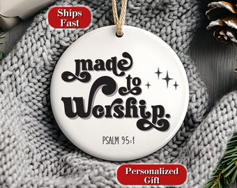 Puede incluir: Adorno de disco de cerámica blanca con las palabras "Made to Worship" en escritura negra y el versículo bíblico Salmo 95:1. El adorno tiene una cuerda dorada para colgar y está sobre un fondo de punto gris.