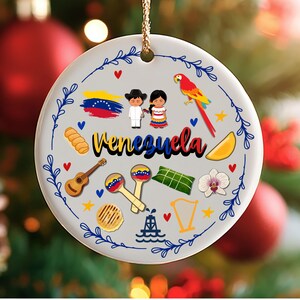 May include: A round ceramic ornament featuring the word "Venezuela" in black script. The ornament is decorated with Venezuelan cultural symbols, including a flag, traditional clothing, a parrot, and musical instruments. A blue floral border surrounds the design.