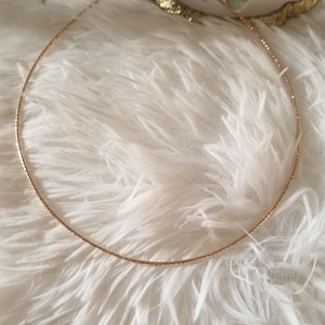 May include: A fine gold-coloured necklace with a textured chain. The necklace is presented on a fluffy, white surface, with a gold bracelet and green sprig in the background. The jewellery is simple and elegant.