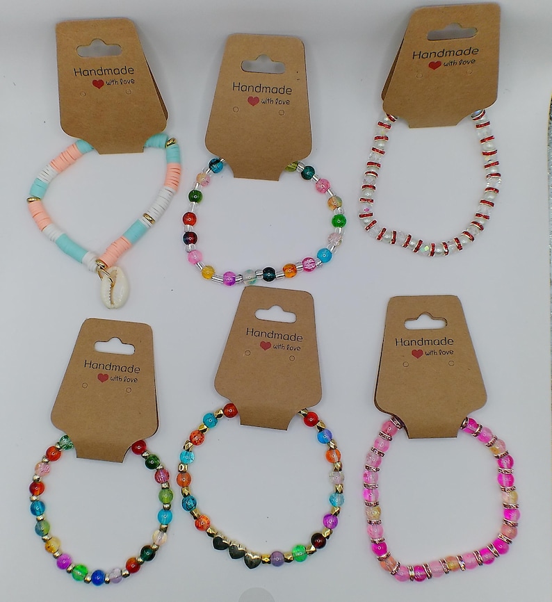 Op de afbeelding: Assortiment van kleurrijke kralenarmbanden met gouden accenten. Elke armband is handgemaakt en wordt geleverd met een bruin kaartje met de tekst "Handmade with love".