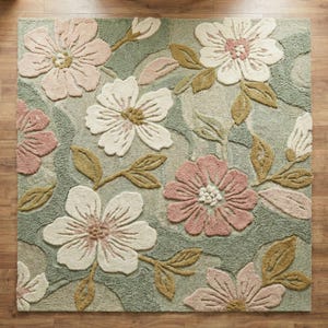 May include: A square rug with a floral design. The rug displays large, textured flowers in pink and white, set against a light green backdrop. The flowers are surrounded by olive green leaves and stems, creating a botanical pattern.