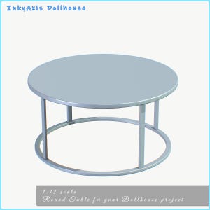 May include: A light gray round table for a dollhouse project. The table has a circular top and a matching circular base connected by vertical supports. The text "InkyAxis Dollhouse" is at the top, and "1:12 scale Round Table for your Dollhouse project" is at the bottom.