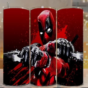 Pode incluir: Um copo vermelho e preto com o personagem da Marvel Comics, Deadpool. O design mostra Deadpool em seu traje, com um fundo vermelho e preto. O copo tem uma palhinha prateada e uma tampa.