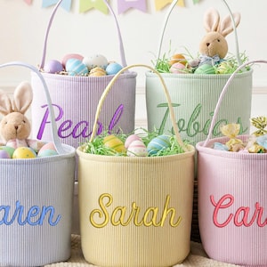以下が含まれることがあります： 刺繍された名前が付いた、パステルカラーのイースターバスケットが5つ。各バスケットには、装飾用の卵、人工芝、ぬいぐるみウサギ、または包装されたお菓子が入っています。バスケットにはハンドルがあり、縦縞模様で装飾されています。