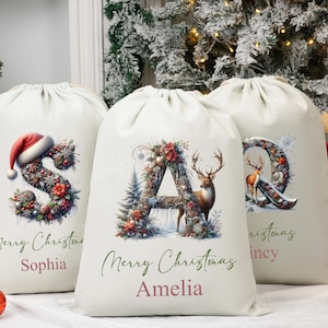 May include: Three off-white Christmas gift bags with drawstring closures. Each bag features a letter decorated with festive floral arrangements and a deer. The bags are personalised with names and the words "Merry Christmas".