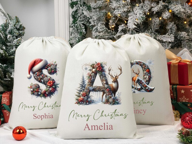 May include: Three off-white Christmas gift bags with drawstring closures. Each bag features a letter decorated with festive floral arrangements and a deer. The bags are personalised with names and the words "Merry Christmas".