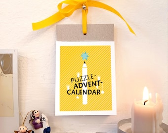 May include: A yellow and white Puzzle Advent Calendar with a yellow ribbon. The calendar features a pencil design with a star on top and the text "PUZZLE-ADVENT-CALENDAR". A lit candle and decorative figurines are also visible.