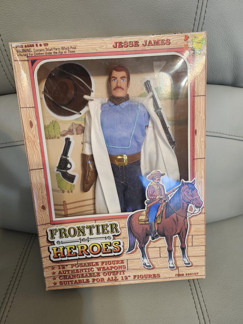 Puede incluir: Una figura de acci&oacute;n de Jesse James "Frontier Heroes" en caja. La figura lleva una camisa azul, vaqueros y un abrigo blanco. La caja incluye un rifle, una pistola y un sombrero de vaquero. La caja tambi&eacute;n presenta un dibujo de un vaquero a caballo.