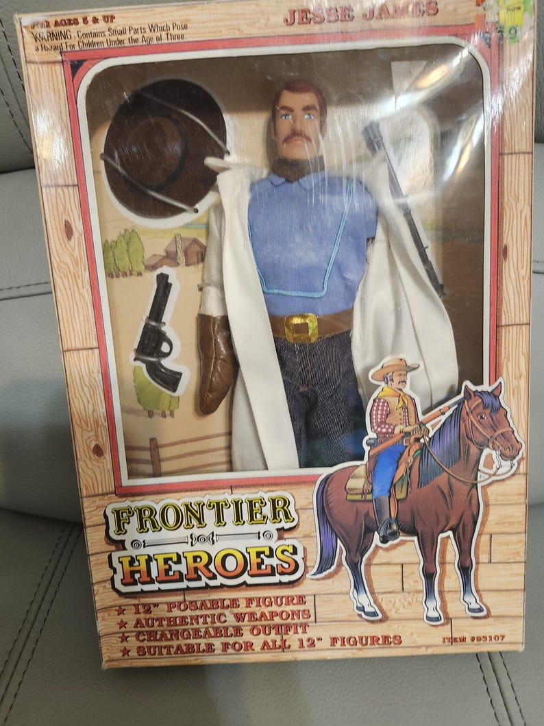 Puede incluir: Figura de acci&oacute;n de Jesse James de 30 cm de Frontier Heroes en caja. La figura viste camisa azul, vaqueros y abrigo blanco. Accesorios: sombrero, pistola y botas. La caja muestra un dibujo de un vaquero a caballo.
