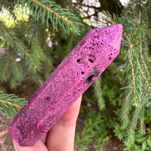 May include: A pink and black, rough-textured, pointed crystal. The crystal is about 6 inches long and has a natural, irregular shape.