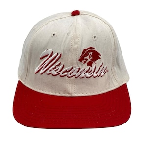 May include: Cream-colored baseball cap with a red brim and button. The word "Wisconsin" is embroidered in red script, along with a red badger logo. A classic, sporty accessory.