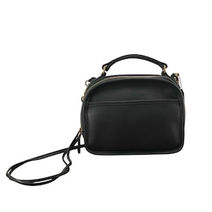 May include: Black leather crossbody bag with a top handle and a long, adjustable strap. The bag has a rounded shape with a zippered main compartment and a front pocket. Gold-toned hardware accents the bag.