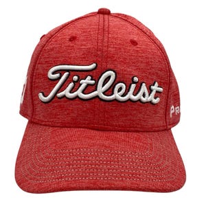 May include: Red Titleist golf hat with white embroidered lettering. The hat has a curved brim and a textured fabric. The word "Titleist" is prominently displayed across the front. The hat is a sporty accessory.