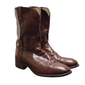 May include: A pair of brown leather cowboy boots. The boots feature a classic design with a pointed toe, a mid-height shaft, and a stacked heel. The leather has a glossy finish.