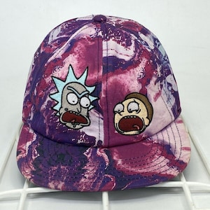 May include: A baseball cap with a vibrant purple and pink marbled pattern. The cap features embroidered cartoon characters on the front. The characters are Rick and Morty, with their faces showing expressions of surprise and shock.