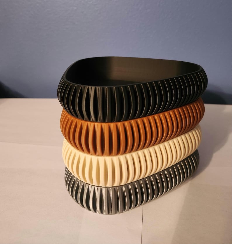 May include: Four stackable, ribbed, oval-shaped, plastic containers in black, brown, cream, and gray.
