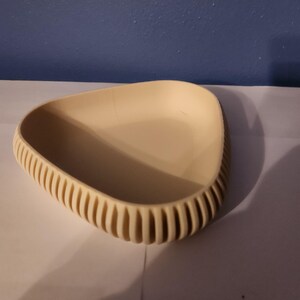 May include: A triangular, cream-colored dish with a textured rim. The dish is made of a smooth, hard material and has a slightly curved bottom.