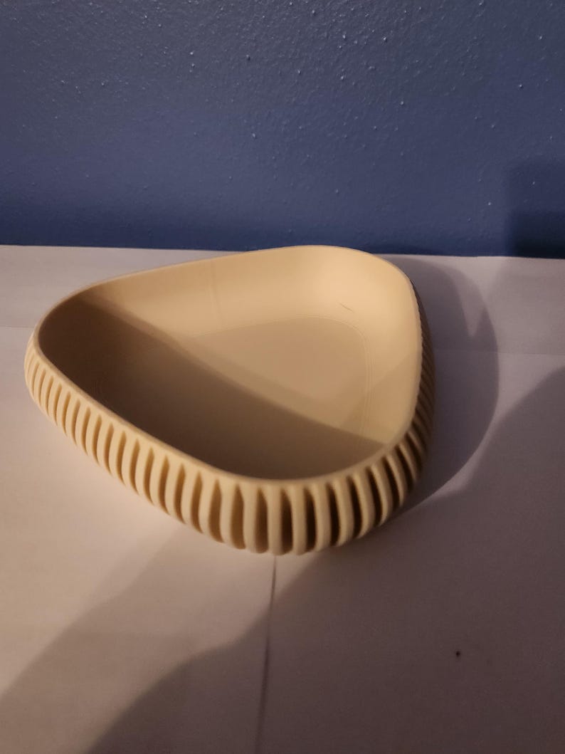 May include: A triangular, cream-colored dish with a textured rim. The dish is made of a smooth, hard material and has a slightly curved bottom.