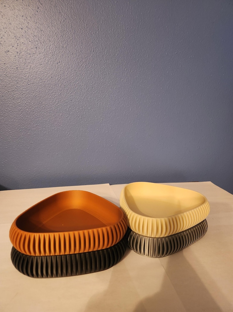May include: Three triangular shaped dishes, one brown, one beige, and one gray, are stacked on a white surface. The dishes have a textured, ribbed design.