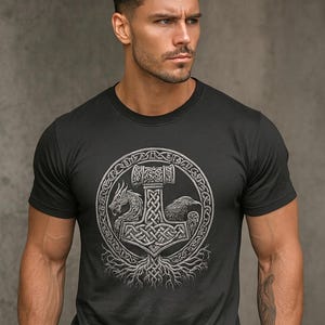 May include: Black t-shirt featuring a detailed silver graphic of Thor's hammer, a dragon, and a raven within a circular design. The design is rooted in a tree-like structure. The shirt is a crew neck style.