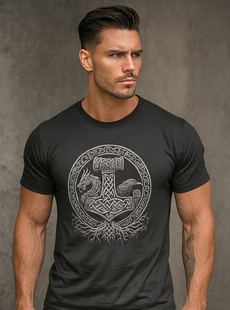 May include: Black t-shirt featuring a detailed silver graphic of Thor's hammer, a dragon, and a raven within a circular design. The design is rooted in a tree-like structure. The shirt is a crew neck style.